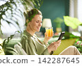 Smiling Woman Relaxing at Home with Juice and Phone 142287645
