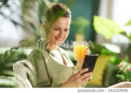 Woman Enjoying Fresh Juice and Phone in Sunlit Room Woman Enjoying Fresh Juice and Phone in Sunlit Room 142287646