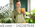 Smiling Woman with Orange Juice and Indoor Plants 142287648