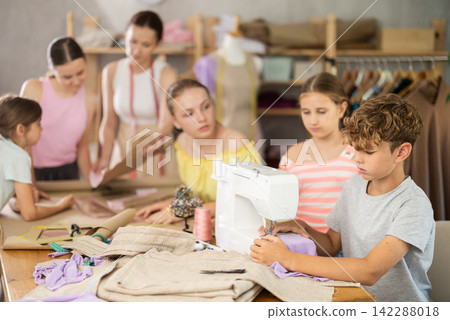 Girl child watches male classmates sew and creating clothes Girl child watches male classmates sew and creating clothes 142288018