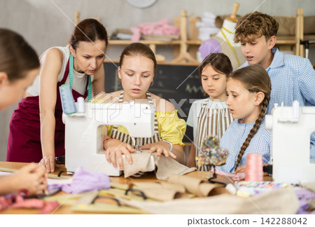 Teenage girl tries to sew surrounded by classmates, female teacher comments and help 142288042
