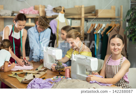Sewing lesson - a group of teenage children learn to sew on sewing machine and cut fabric 142288087