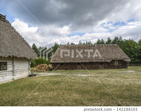Thatched Barn And Rustic Farmhouses In Rural Countryside With Haystack And Wooden Outbuildings 142288103