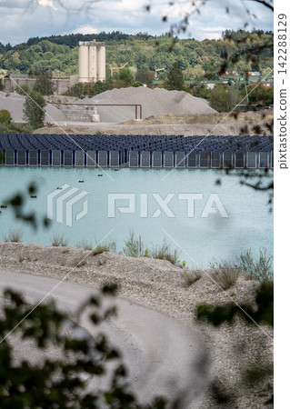 Vertical floating solar panels on the Gilching quarry lake in Bavaria, Germany, beside a gravel and crushing plant, renewable energy infrastructure, industrial landscape and innovative clean Vertical floating solar panels on the Gilching quarry lake in Bavaria, Germany, beside a gravel and crushing plant, renewable energy infrastructure, industrial landscape and innovative clean 142288129