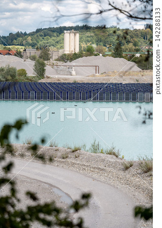 Vertical floating solar panels on the Gilching quarry lake in Bavaria, Germany, beside a gravel and crushing plant, renewable energy infrastructure, industrial landscape and innovative clean Vertical floating solar panels on the Gilching quarry lake in Bavaria, Germany, beside a gravel and crushing plant, renewable energy infrastructure, industrial landscape and innovative clean 142288133
