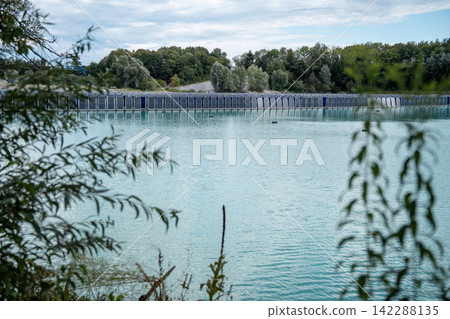 Vertical floating solar panels on the Gilching quarry lake in Bavaria, Germany, beside a gravel and crushing plant, renewable energy infrastructure, industrial landscape and innovative clean Vertical floating solar panels on the Gilching quarry lake in Bavaria, Germany, beside a gravel and crushing plant, renewable energy infrastructure, industrial landscape and innovative clean 142288135