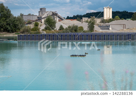 Vertical floating solar panels on the Gilching quarry lake in Bavaria, Germany, beside a gravel and crushing plant, renewable energy infrastructure, industrial landscape and innovative clean Vertical floating solar panels on the Gilching quarry lake in Bavaria, Germany, beside a gravel and crushing plant, renewable energy infrastructure, industrial landscape and innovative clean 142288136