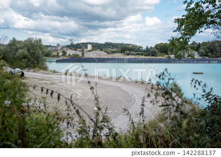 Vertical floating solar panels on the Gilching quarry lake in Bavaria, Germany, beside a gravel and crushing plant, renewable energy infrastructure, industrial landscape and innovative clean Vertical floating solar panels on the Gilching quarry lake in Bavaria, Germany, beside a gravel and crushing plant, renewable energy infrastructure, industrial landscape and innovative clean 142288137
