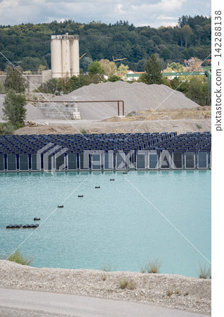 Vertical floating solar panels on the Gilching quarry lake in Bavaria, Germany, beside a gravel and crushing plant, renewable energy infrastructure, industrial landscape and innovative clean Vertical floating solar panels on the Gilching quarry lake in Bavaria, Germany, beside a gravel and crushing plant, renewable energy infrastructure, industrial landscape and innovative clean 142288138