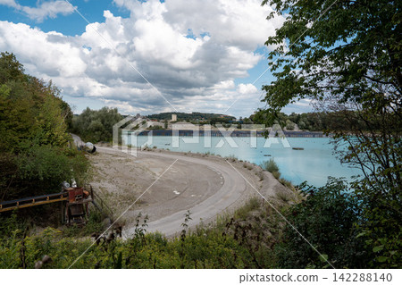 Vertical floating solar panels on the Gilching quarry lake in Bavaria, Germany, beside a gravel and crushing plant, renewable energy infrastructure, industrial landscape and innovative clean Vertical floating solar panels on the Gilching quarry lake in Bavaria, Germany, beside a gravel and crushing plant, renewable energy infrastructure, industrial landscape and innovative clean 142288140