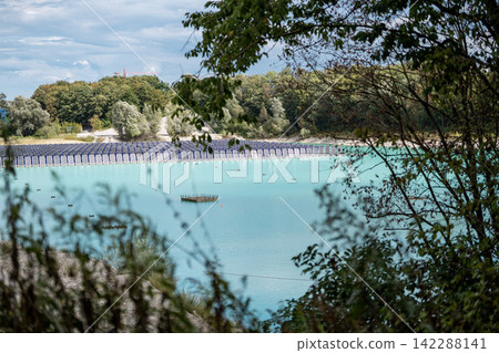 Vertical floating solar panels on the Gilching quarry lake in Bavaria, Germany, beside a gravel and crushing plant, renewable energy infrastructure, industrial landscape and innovative clean Vertical floating solar panels on the Gilching quarry lake in Bavaria, Germany, beside a gravel and crushing plant, renewable energy infrastructure, industrial landscape and innovative clean 142288141