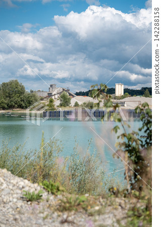 Vertical floating solar panels on the Gilching quarry lake in Bavaria, Germany, beside a gravel and crushing plant, renewable energy infrastructure, industrial landscape and innovative clean Vertical floating solar panels on the Gilching quarry lake in Bavaria, Germany, beside a gravel and crushing plant, renewable energy infrastructure, industrial landscape and innovative clean 142288158