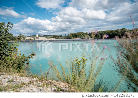 Vertical floating solar panels on the Gilching quarry lake in Bavaria, Germany, beside a gravel and crushing plant, renewable energy infrastructure, industrial landscape and innovative clean Vertical floating solar panels on the Gilching quarry lake in Bavaria, Germany, beside a gravel and crushing plant, renewable energy infrastructure, industrial landscape and innovative clean 142288173