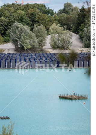 Vertical floating solar panels on the Gilching quarry lake in Bavaria, Germany, beside a gravel and crushing plant, renewable energy infrastructure, industrial landscape and innovative clean Vertical floating solar panels on the Gilching quarry lake in Bavaria, Germany, beside a gravel and crushing plant, renewable energy infrastructure, industrial landscape and innovative clean 142288198