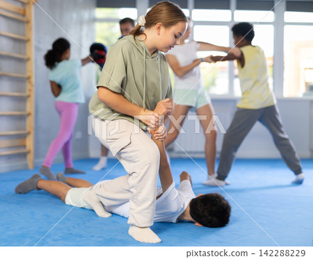 Tween girl applying armlock to face-down boy in mock fight at self-defense classes Tween girl applying armlock to face-down boy in mock fight at self-defense classes 142288229