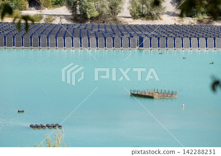 Vertical floating solar panels on the Gilching quarry lake in Bavaria, Germany, beside a gravel and crushing plant, renewable energy infrastructure, industrial landscape and innovative clean Vertical floating solar panels on the Gilching quarry lake in Bavaria, Germany, beside a gravel and crushing plant, renewable energy infrastructure, industrial landscape and innovative clean 142288231