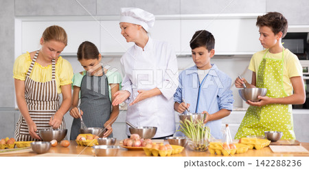 Team of positive teenagers and female chef at cooking classes. Learn to beat raw eggs Team of positive teenagers and female chef at cooking classes. Learn to beat raw eggs 142288236