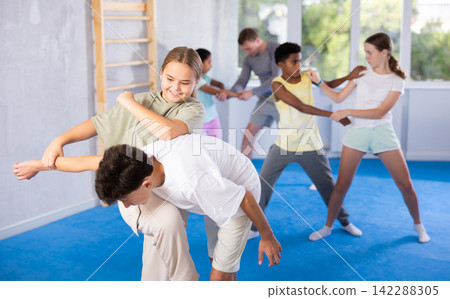 Preteen girl performing elbow and knee strikes while blocking arm of boy in mock fight Preteen girl performing elbow and knee strikes while blocking arm of boy in mock fight 142288305