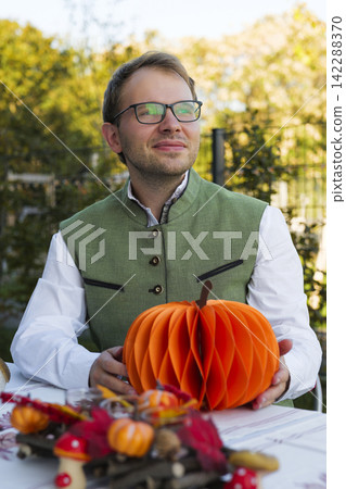 Man sitting at an autumn table and holding a paper pumpkin, illustrating Bavarian style Oktoberfest outdoor celebration. Man sitting at an autumn table and holding a paper pumpkin, illustrating Bavarian style Oktoberfest outdoor celebration. 142288370