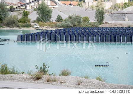 Vertical floating solar panels on the Gilching quarry lake in Bavaria, Germany, beside a gravel and crushing plant, renewable energy infrastructure, industrial landscape and innovative clean Vertical floating solar panels on the Gilching quarry lake in Bavaria, Germany, beside a gravel and crushing plant, renewable energy infrastructure, industrial landscape and innovative clean 142288378