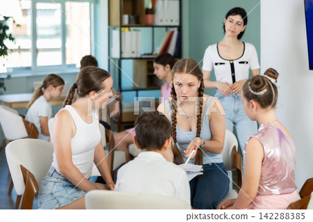 Teenagers and children working in teams on chairs monitored by teacher Teenagers and children working in teams on chairs monitored by teacher 142288385