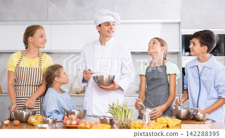 Friendly young chef running culinary courses for group of children Friendly young chef running culinary courses for group of children 142288395