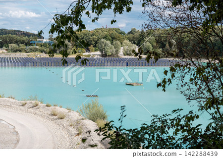 Vertical floating solar panels on the Gilching quarry lake in Bavaria, Germany, beside a gravel and crushing plant, renewable energy infrastructure, industrial landscape and innovative clean Vertical floating solar panels on the Gilching quarry lake in Bavaria, Germany, beside a gravel and crushing plant, renewable energy infrastructure, industrial landscape and innovative clean 142288439