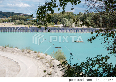 Vertical floating solar panels on the Gilching quarry lake in Bavaria, Germany, beside a gravel and crushing plant, renewable energy infrastructure, industrial landscape and innovative clean Vertical floating solar panels on the Gilching quarry lake in Bavaria, Germany, beside a gravel and crushing plant, renewable energy infrastructure, industrial landscape and innovative clean 142288467