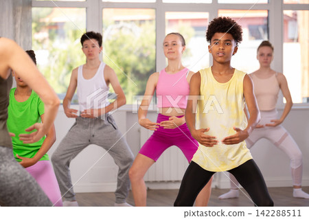 Thin teenage boy practicing plie position of ballet standing in row with others Thin teenage boy practicing plie position of ballet standing in row with others 142288511
