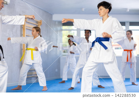Children of different nationalities in kimono standing in fight stance during group karate training in gym 142288530