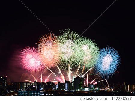 Colorful fireworks bursting in rapid succession against the summer night sky, silhouetted against the city skyline. Colorful fireworks bursting in rapid succession against the summer night sky, silhouetted against the city skyline. 142288557