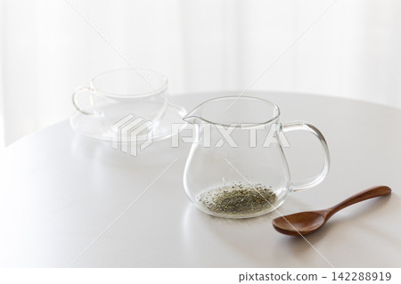 透明玻璃茶壺裡盛著綠茶葉，放在白色桌上。 142288919