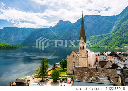 Hallstatt, Austria. The scenery of Lake Hallstatt and the village spread out against the backdrop of a blue sky and the lush green Alps. Hallstatt, Austria. The scenery of Lake Hallstatt and the village spread out against the backdrop of a blue sky and the lush green Alps. 142288948