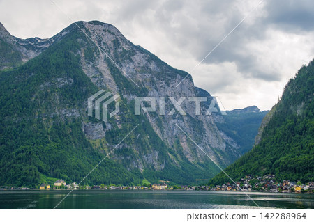 Hallstatt, Austria. Under a cloudy sky, the magnificent natural scenery of Lake Hallstatt and the towering Alps unfolds. Hallstatt, Austria. Under a cloudy sky, the magnificent natural scenery of Lake Hallstatt and the towering Alps unfolds. 142288964