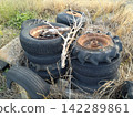 A pile of old tires and rusty wheels left abandoned in the grass (illegal dumping/waste). 142289861