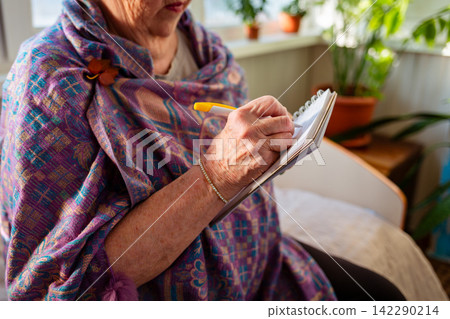 Senior Caucasian woman documents ideas and important plans in her notebook. She creates a structured daily routine with effective time management techniques. Close up Senior Caucasian woman documents ideas and important plans in her notebook. She creates a structured daily routine with effective time management techniques. Close up 142290214