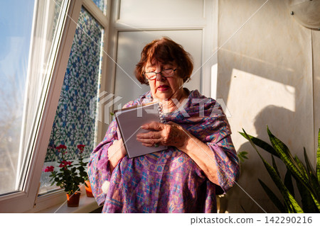 Elderly woman writes a checklist in a notebook while sitting in a comfortable room. She stays motivated by learning and organizing her personal responsibilities. Elderly woman writes a checklist in a notebook while sitting in a comfortable room. She stays motivated by learning and organizing her personal responsibilities. 142290216
