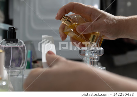 Hand sprays fragrance from glass perfume bottle on the dressing table vanity Hand sprays fragrance from glass perfume bottle on the dressing table vanity 142290458