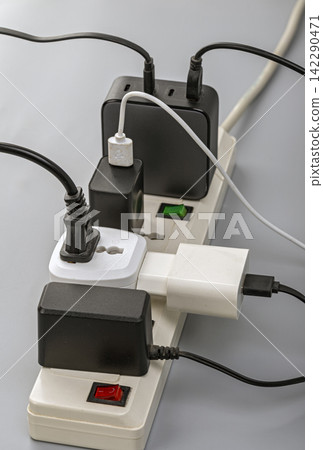 Close-up view of a crowded power strip overloaded with black and white chargers, USB adapters, and tangled cables, illustrating electrical safety hazards and outlet overuse Close-up view of a crowded power strip overloaded with black and white chargers, USB adapters, and tangled cables, illustrating electrical safety hazards and outlet overuse 142290471