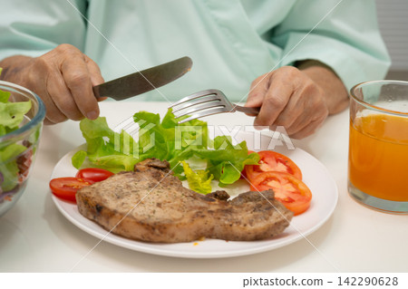 Asian elderly woman patient eating salmon stake and vegetable salad for healthy food in hospital. 142290628