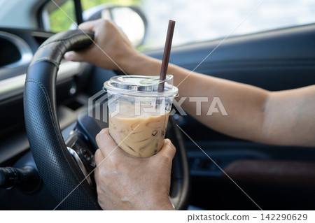 Asian lady holding ice coffee to eat in car, dangerous and risk an accident. Asian lady holding ice coffee to eat in car, dangerous and risk an accident. 142290629
