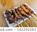 A delicious-looking assortment of yakitori (grilled chicken skewers) from an izakaya (Japanese pub) menu is laid out on a wood-grained table. 142291563
