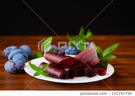 Homemade plum fruit leather rolls with fresh plums on wooden table Homemade plum fruit leather rolls with fresh plums on wooden table 142291794