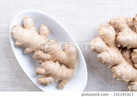 Fresh ginger root, in oval white bowl on linen. Rhizomes of Zingiber officinale, used in cooking for its flavor, and in traditional folk medicine to relieve nausea, and reduce inflammation. Photo Fresh ginger root, in oval white bowl on linen. Rhizomes of Zingiber officinale, used in cooking for its flavor, and in traditional folk medicine to relieve nausea, and reduce inflammation. Photo 142291921