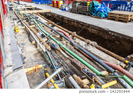 Exposed utility lines and pipes in street construction trench Exposed utility lines and pipes in street construction trench 142291944