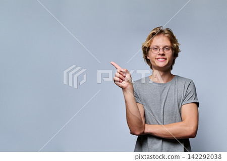 Portrait of smiling teenage student in glasses pointing finger aside Portrait of smiling teenage student in glasses pointing finger aside 142292038