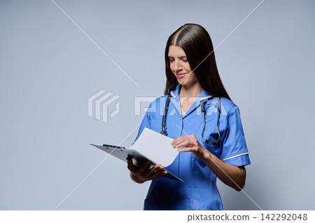 Female nurse turning page on clipboard reading patient records against grey background 142292048
