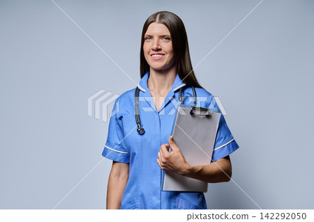 Smiling female UK nurse holding clipboard with stethoscope looking at camera Smiling female UK nurse holding clipboard with stethoscope looking at camera 142292050