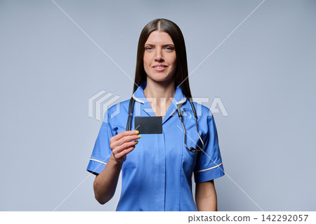 Smiling female nurse holding blank black card standing against grey background Smiling female nurse holding blank black card standing against grey background 142292057
