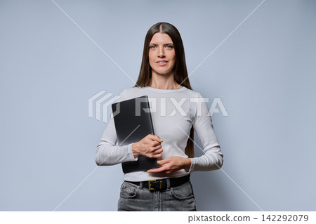 Portrait of happy smiling young woman holding laptop computer on grey background Portrait of happy smiling young woman holding laptop computer on grey background 142292079